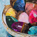 A colorful fabric collage of a bowl full of colorfully painted acorns.  Fall vibes of jewel toned painted acorns.